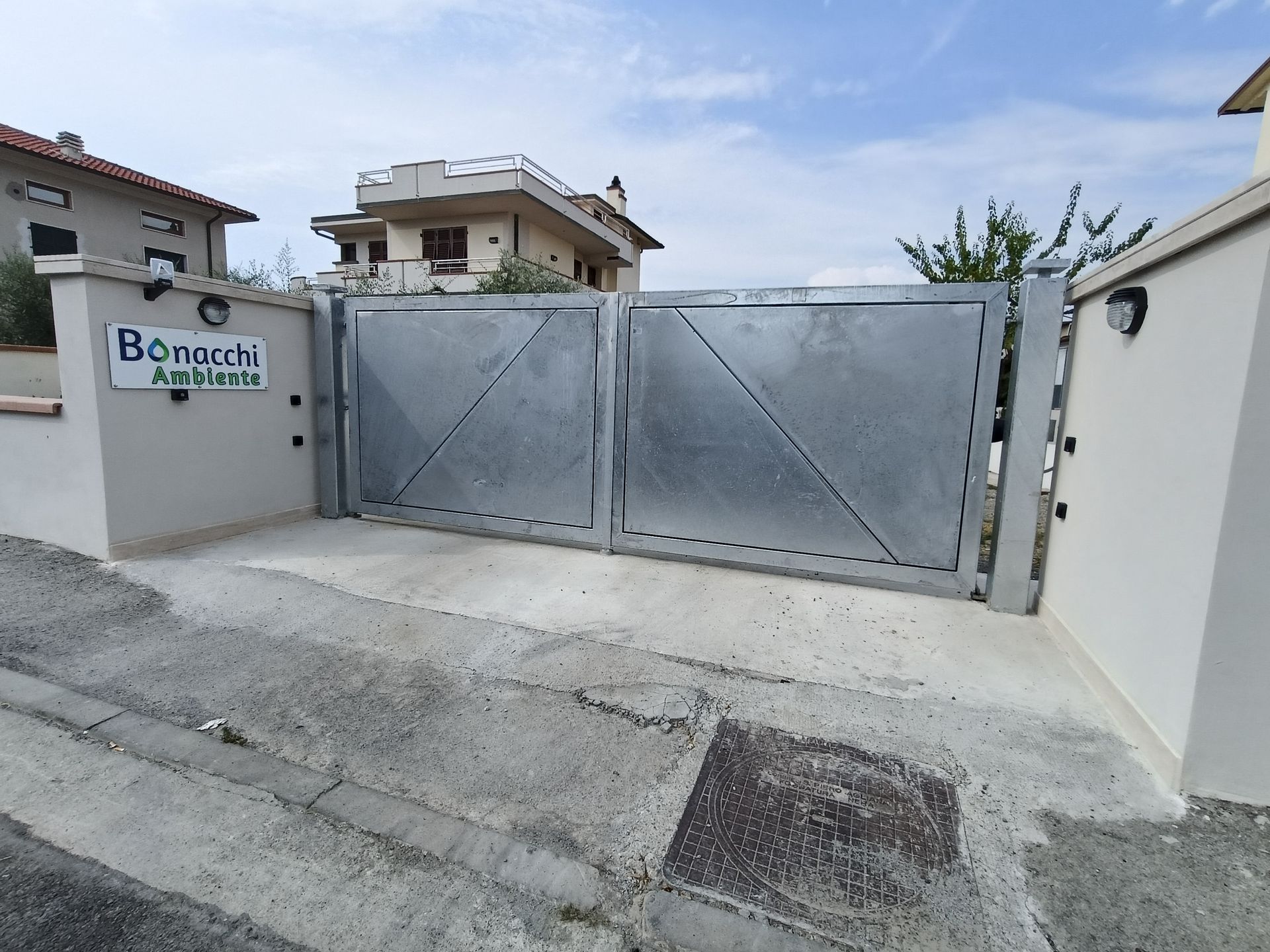 Cancello metallico chiuso all'ingresso di un'abitazione con muro bianco e vialetto pavimentato.