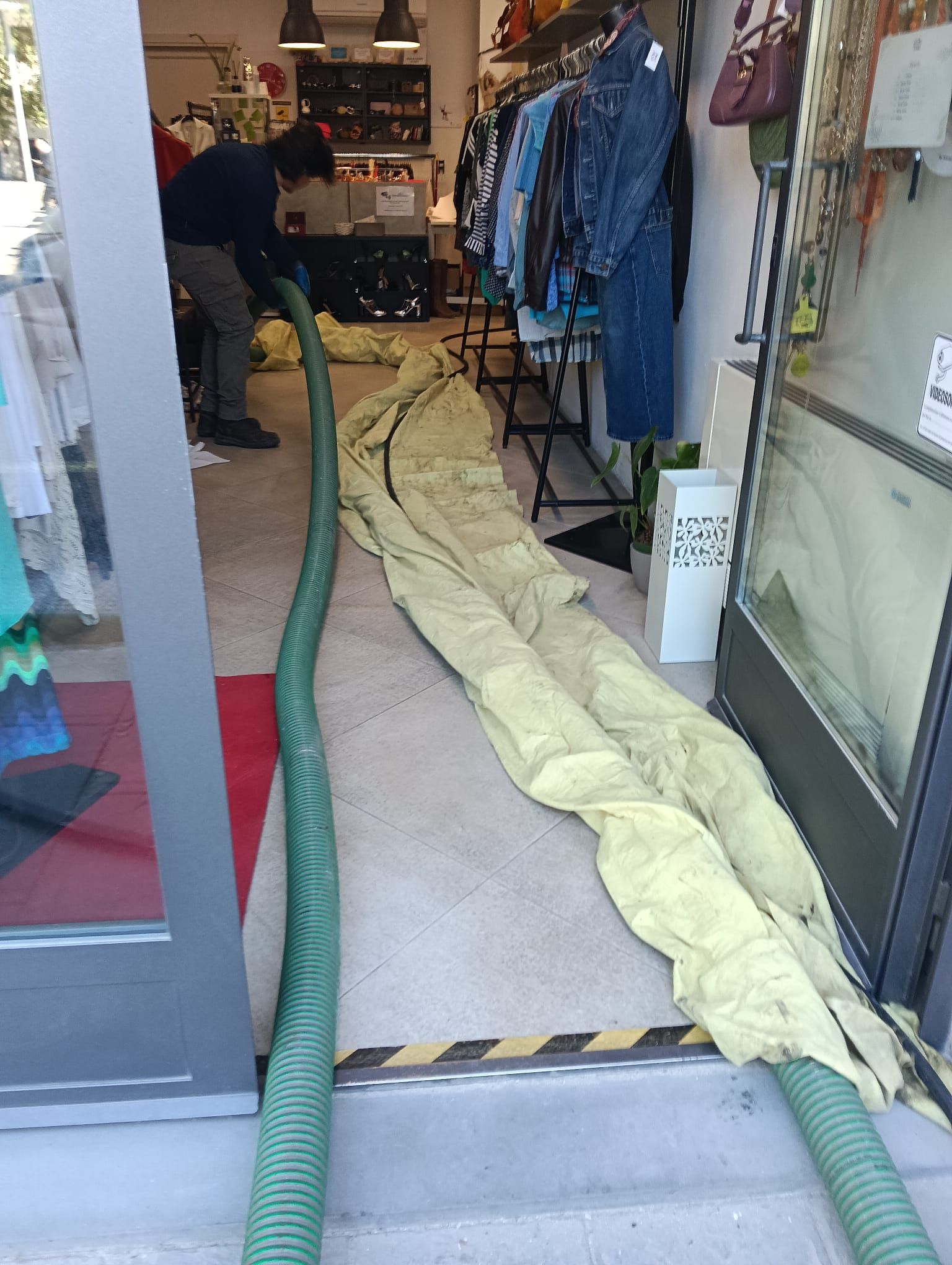 Ingresso del negozio con tubo flessibile e telo protettivo arrotolato steso sulla porta durante le operazioni di pulizia.