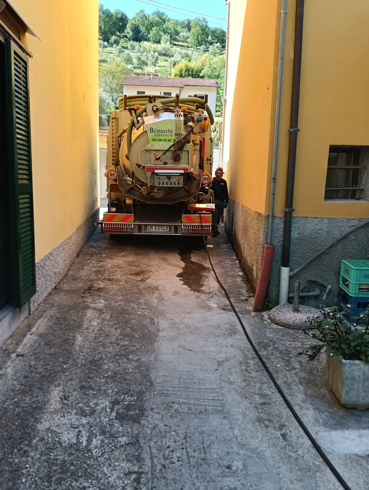 Un'autocisterna in uno stretto vicolo tra edifici gialli, con un operaio in piedi accanto.