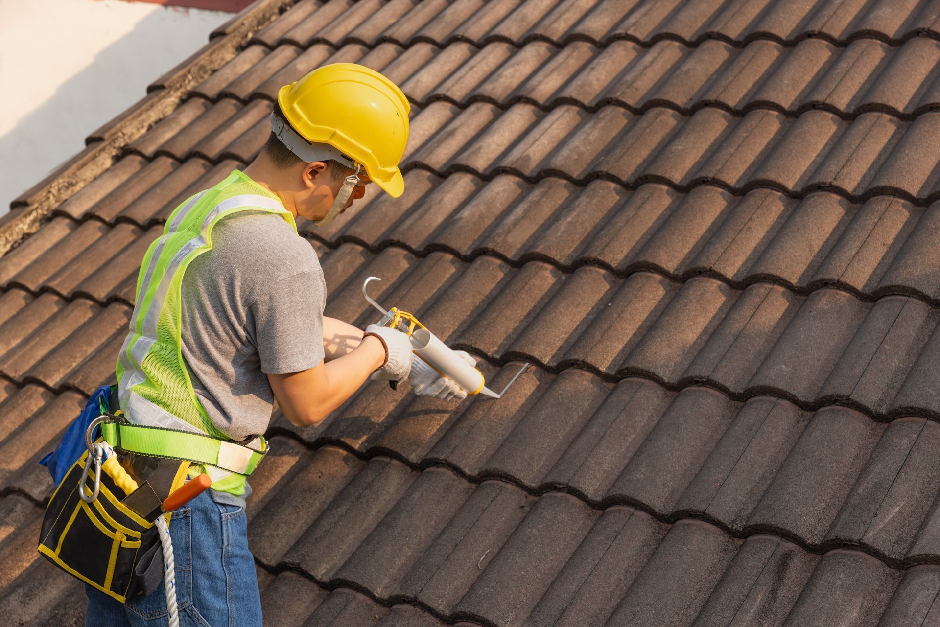 A man wearing a hard hat and safety vest is standing on a tiled roof.