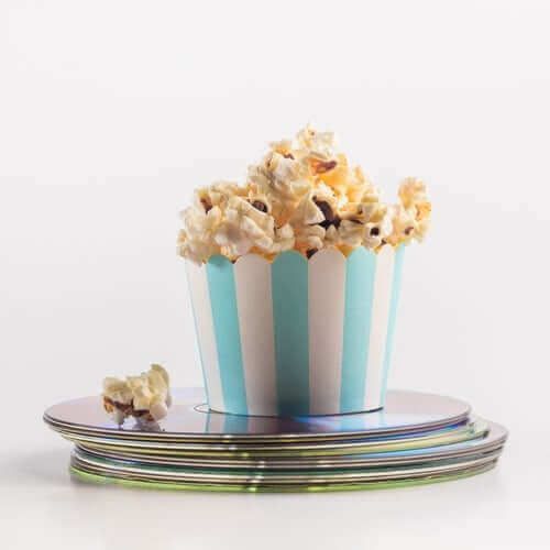 A bucket of popcorn is sitting on top of a stack of cds.