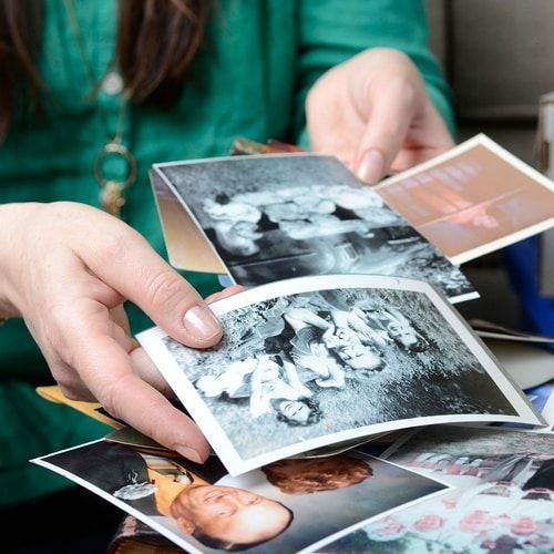 A woman in a green sweater is holding a pile of old photographs