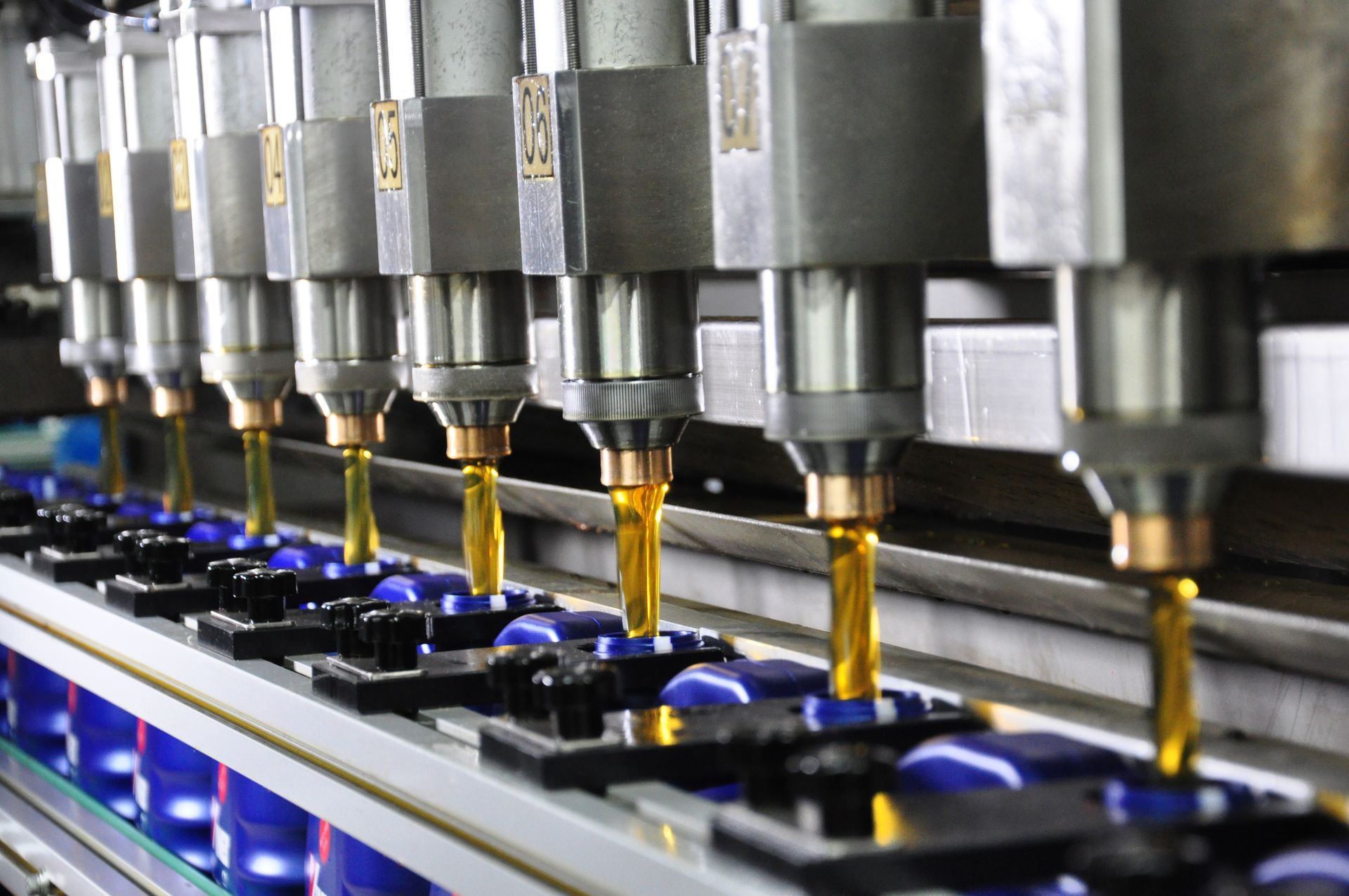 A machine is pouring oil into a row of blue bottles