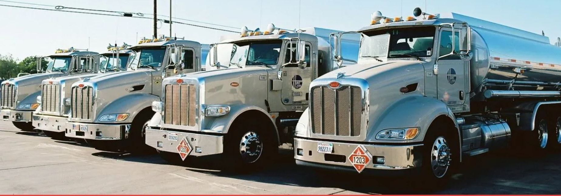A tanker truck is driving down a highway next to a yellow truck.