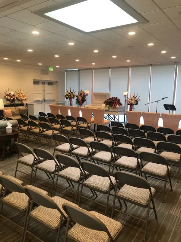 Rows of folding chairs facing a flower-decorated casket in a small funeral chapel.