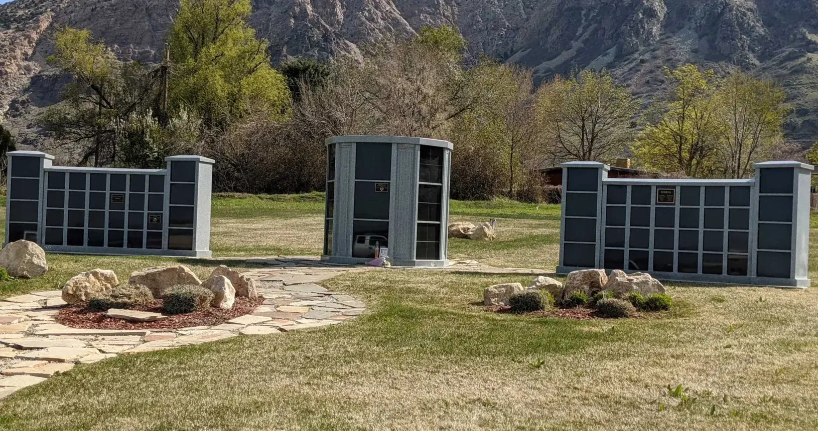 Outdoor compost bins arranged on a grassy yard with rocks and trees in the background