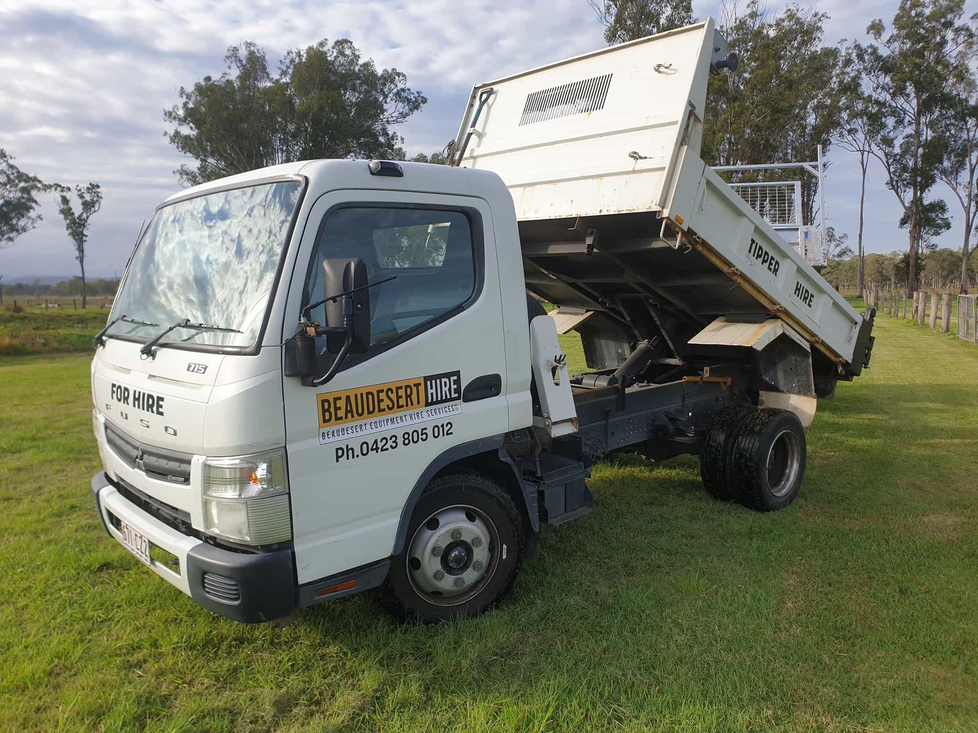 A white dump truck is parked in a grassy field. — Beaudesert Equipment Hire Services in Beaudesert, QLD