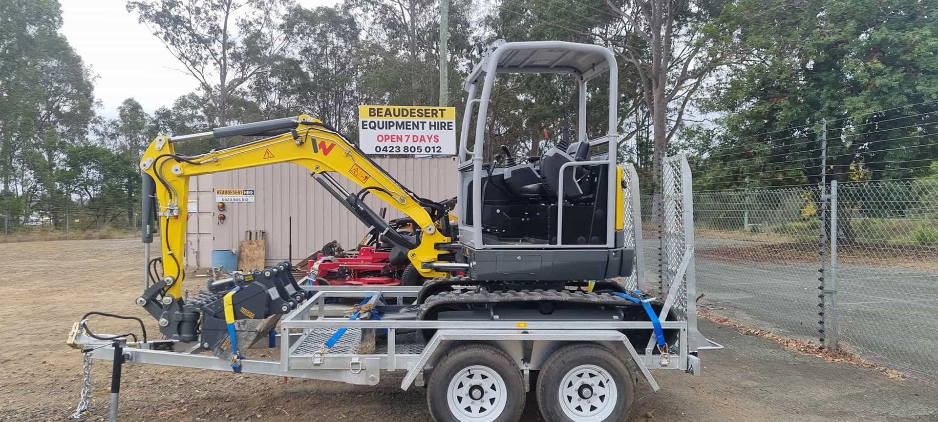 A small excavator is parked on a trailer in a field. — Beaudesert Equipment Hire Services in Beaudesert, QLD