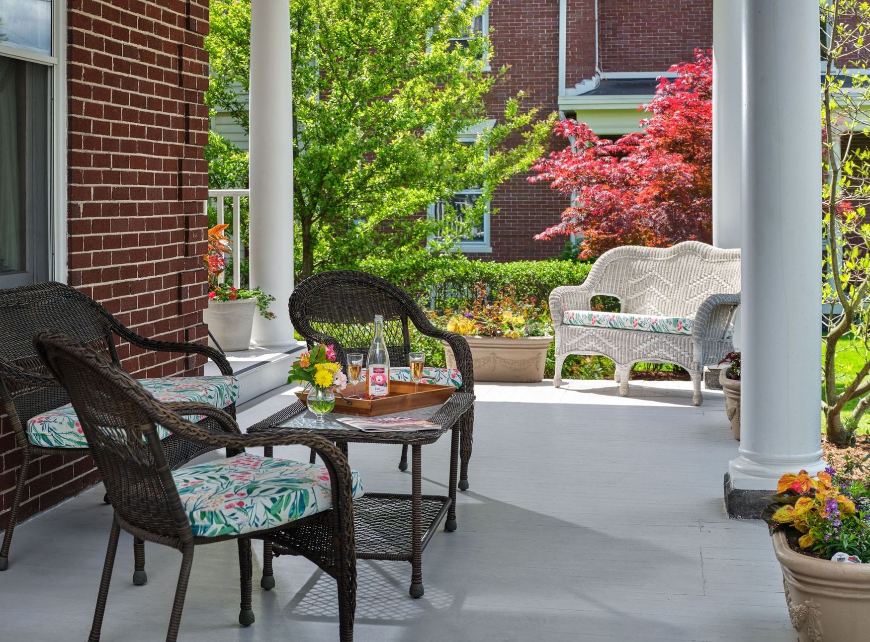 A porch with wicker furniture and a table with wine glasses on it.