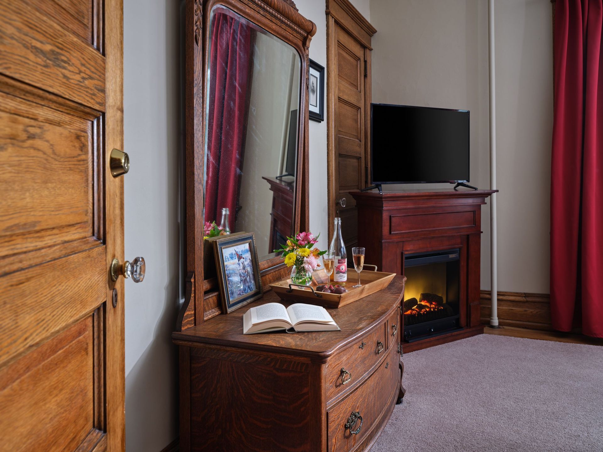 A bedroom with a fireplace , dresser , mirror and television.