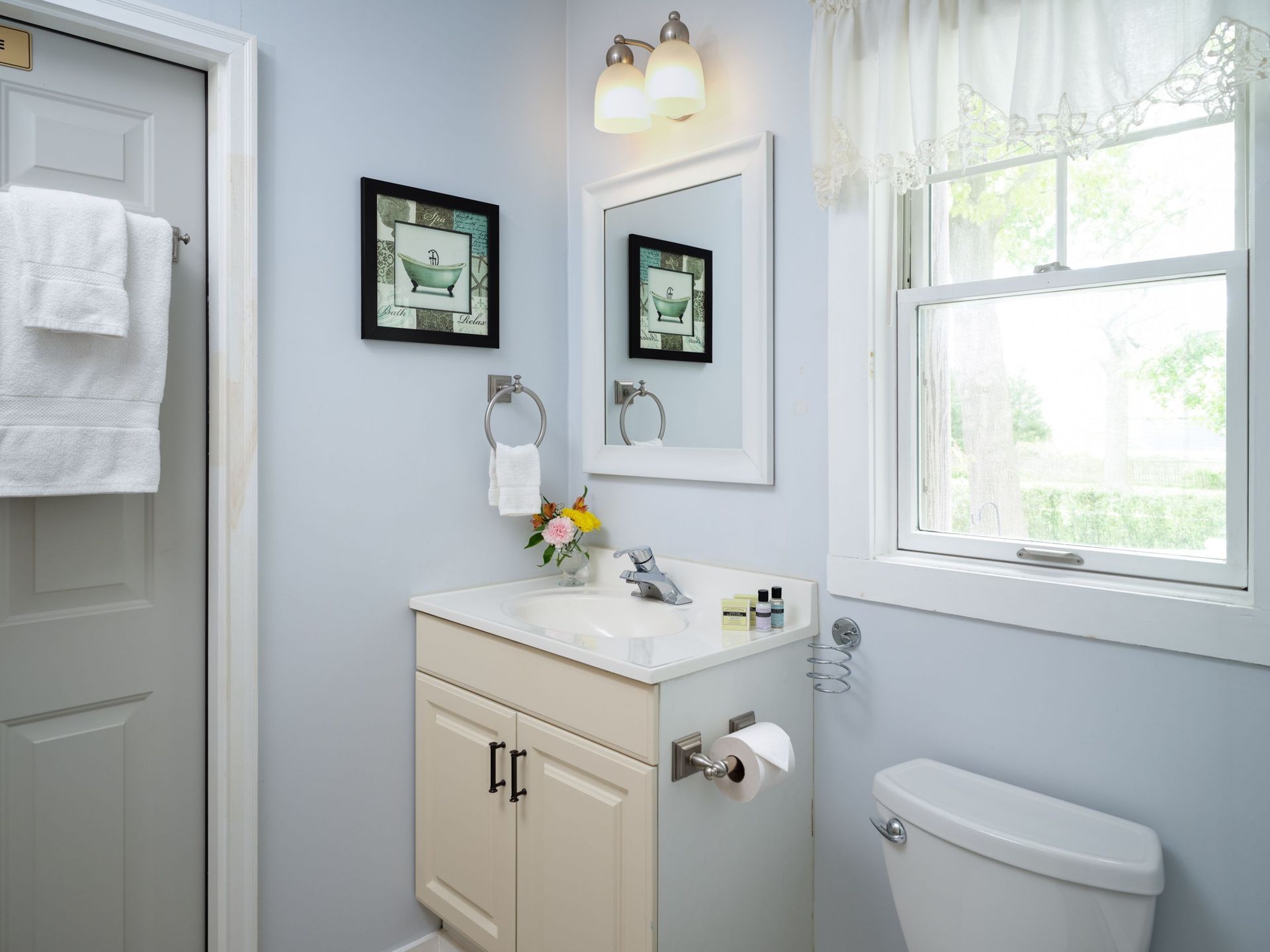 A bathroom with a sink , toilet , mirror and window.