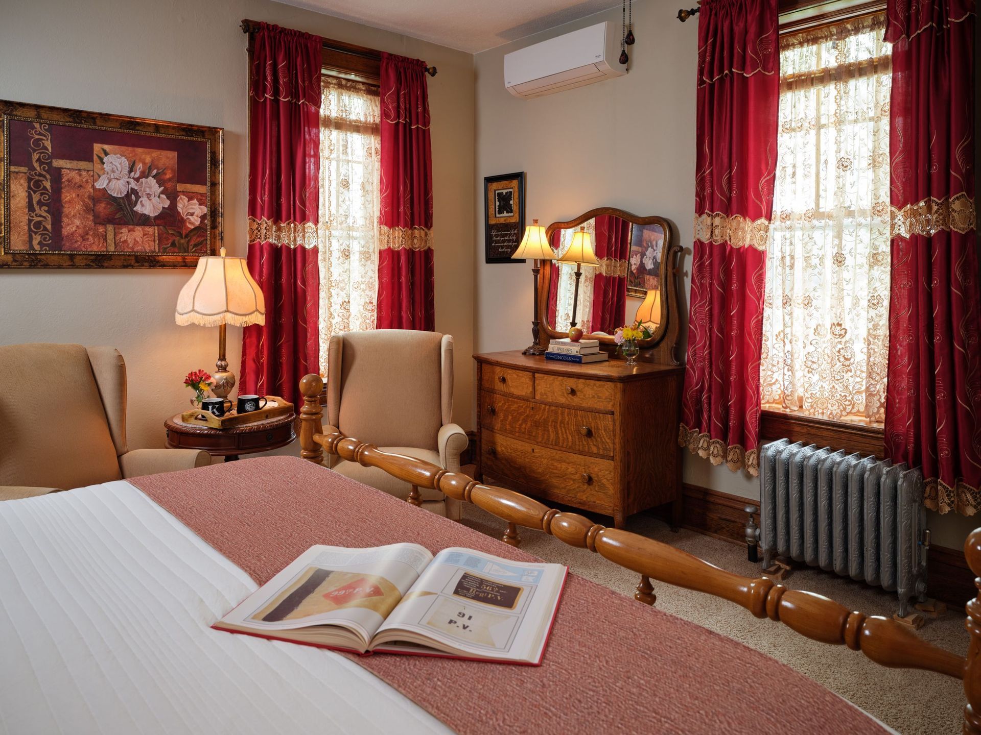 A bedroom with a bed , dresser , chairs and a book on the bed.