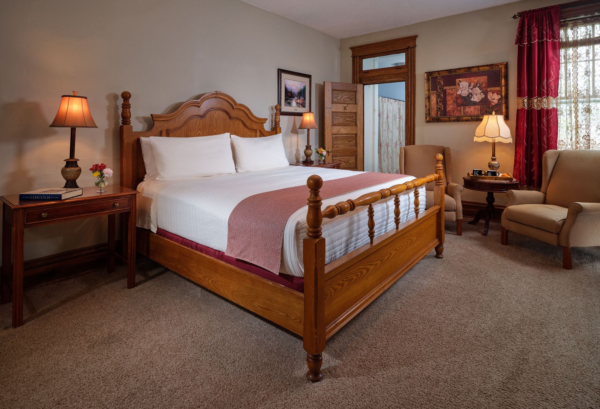 A hotel room with a king size bed , chairs , lamps and a table.