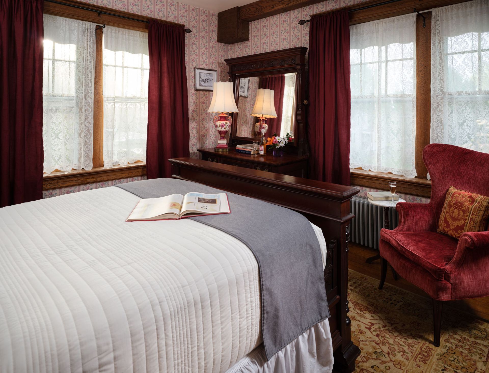 A bedroom with a bed , chair , lamps and a book on the bed.
