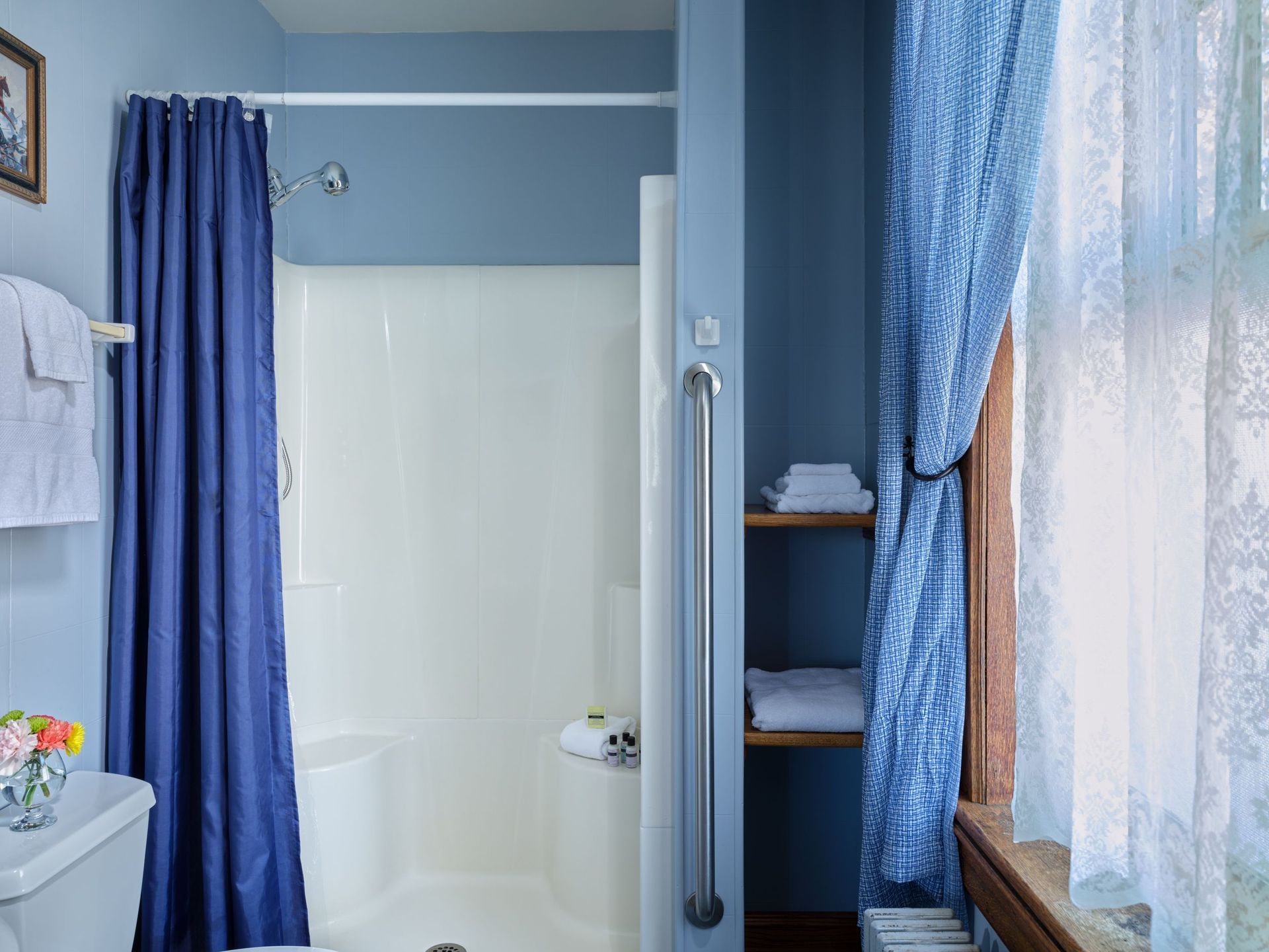 A bathroom with a blue shower curtain , a toilet , and a window.