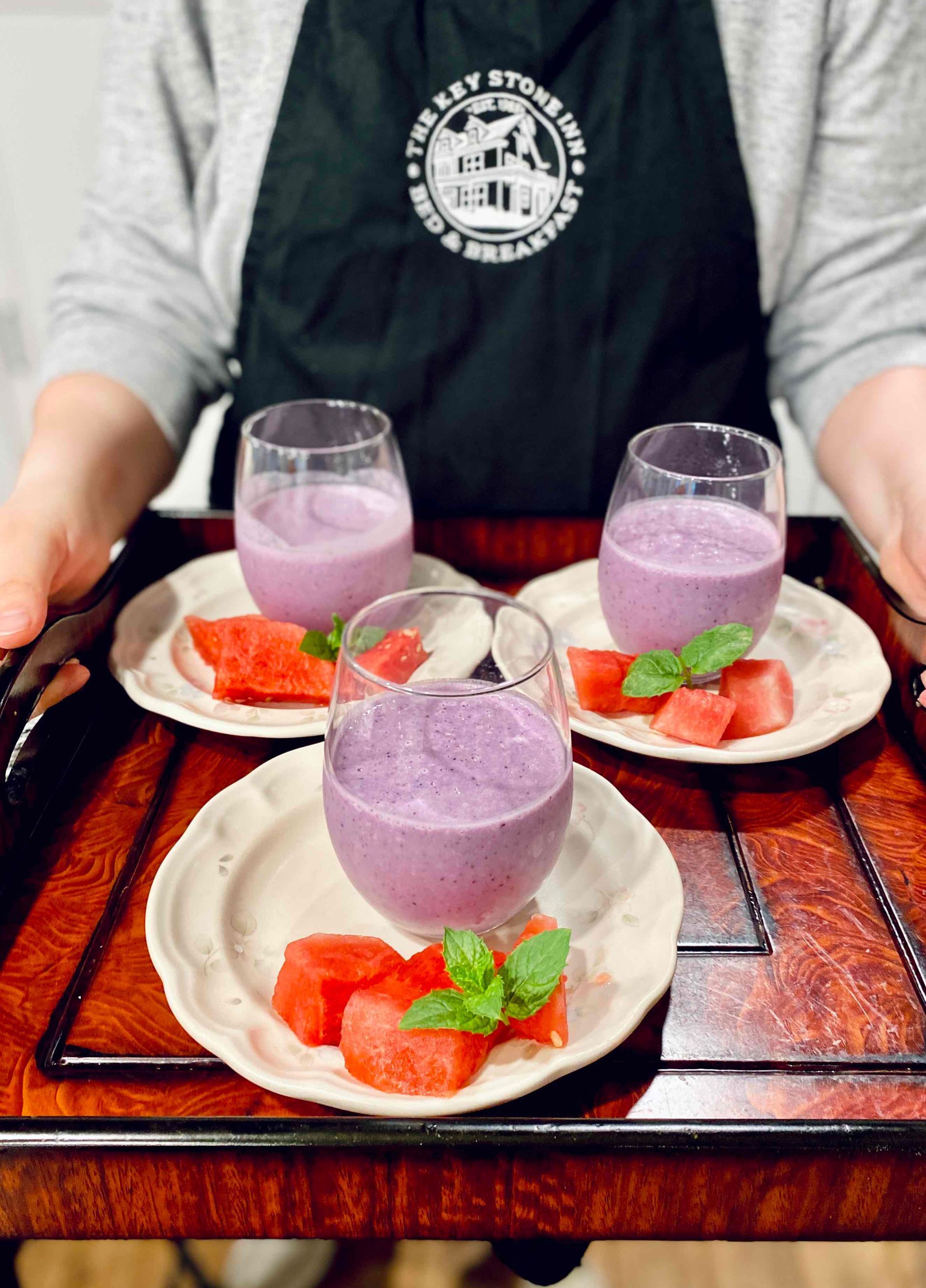 A person wearing an apron is holding a tray of smoothies and watermelon slices