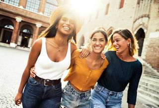 Three women are walking down a street together and smiling.