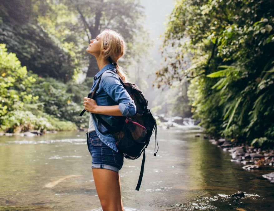 A woman with a backpack is standing in a river.