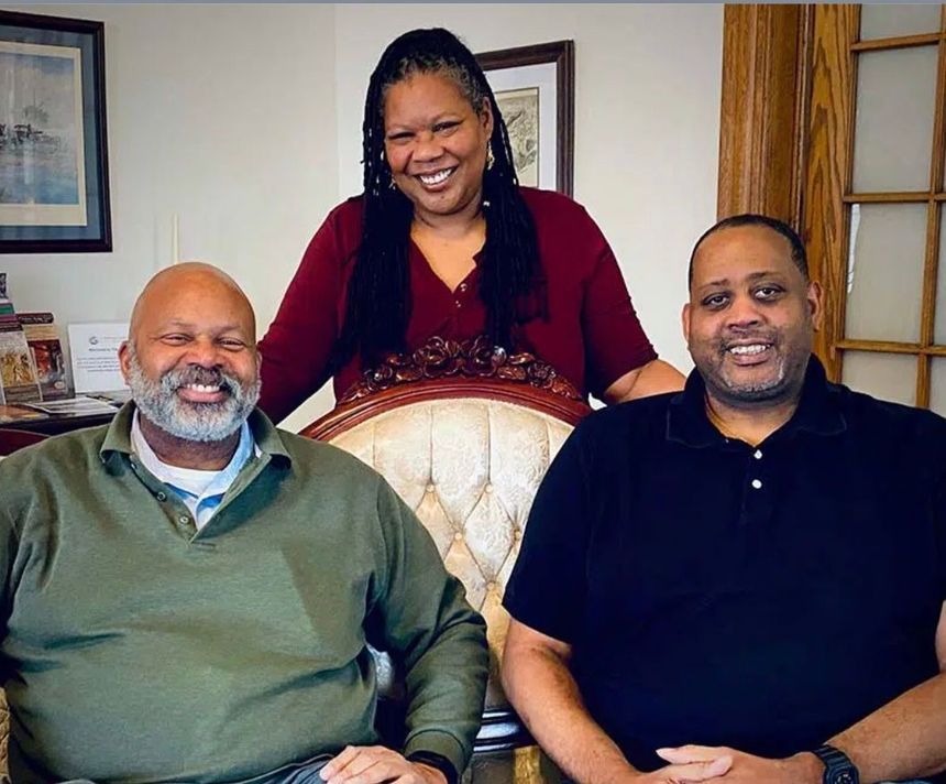 Two men and a woman are posing for a picture in a living room.