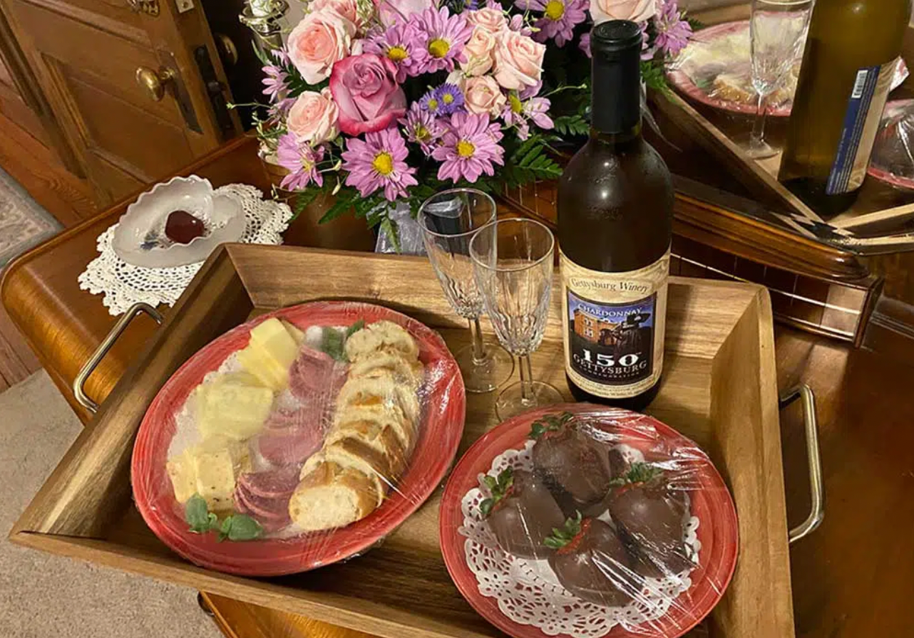 A wooden tray with plates of food and a bottle of wine on a table.