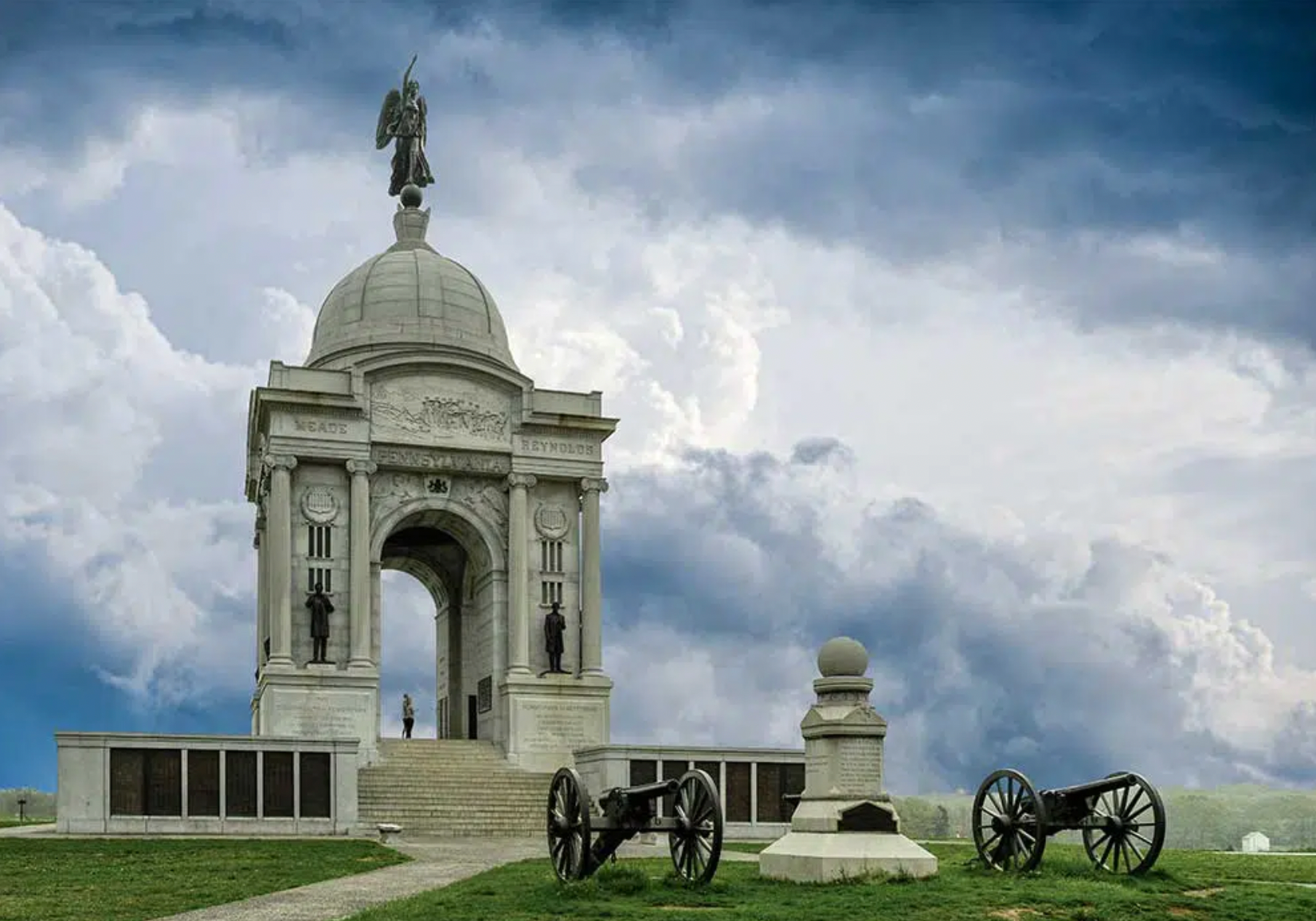 There is a statue of a man on top of a building with a cannon in front of it.