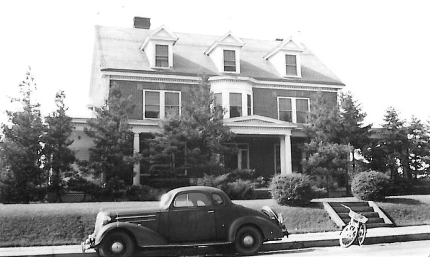 A black and white photo of a car parked in front of a house