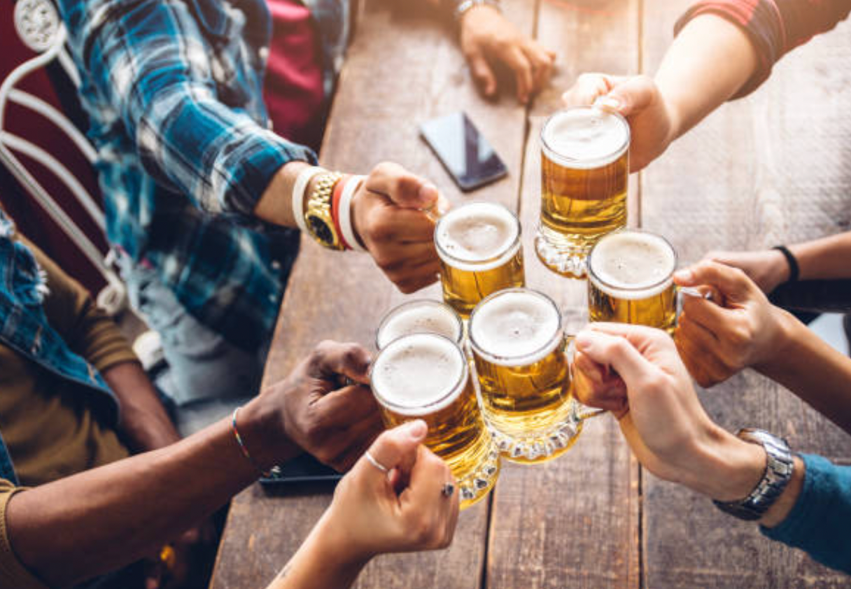 A group of people are toasting with beer glasses at a table.