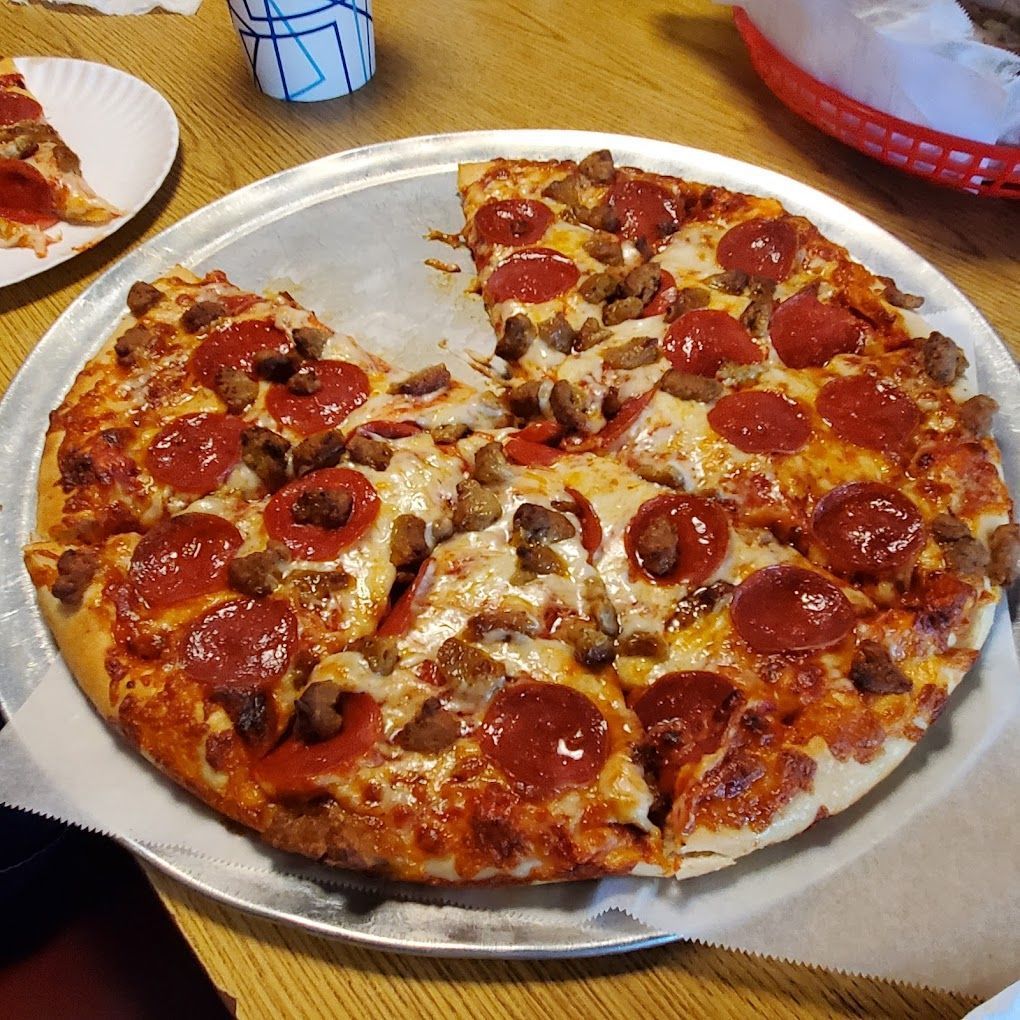 A pepperoni pizza with sausage and mushrooms on a pan on a wooden table.