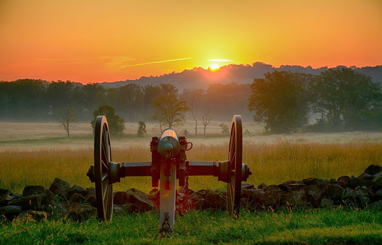 A cannon is sitting in the middle of a field at sunset.