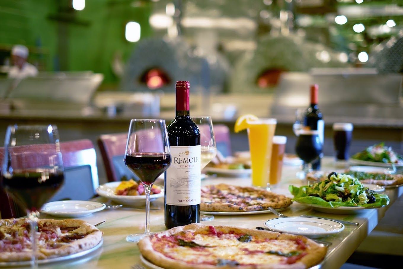 A bottle of wine is sitting on a table with pizzas and glasses of wine.