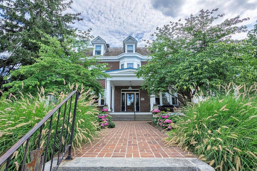A large house with a brick walkway leading to the front door surrounded by trees and bushes.