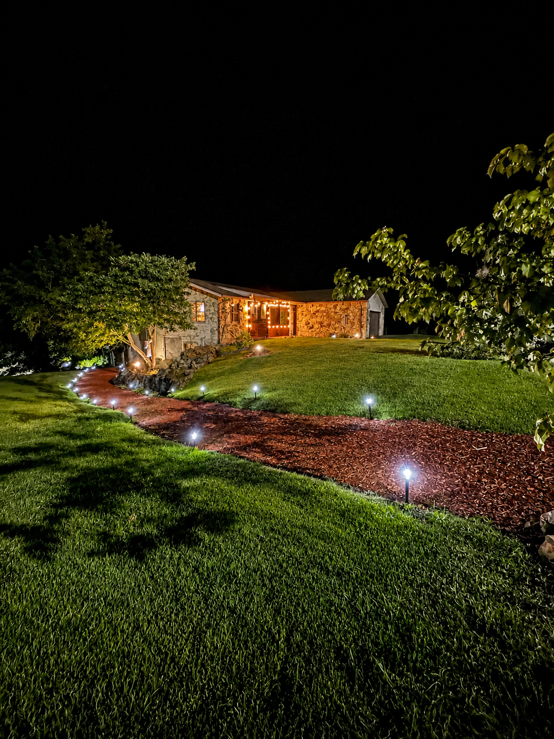 Lit stone house at night with a lit garden path and glowing landscape lights