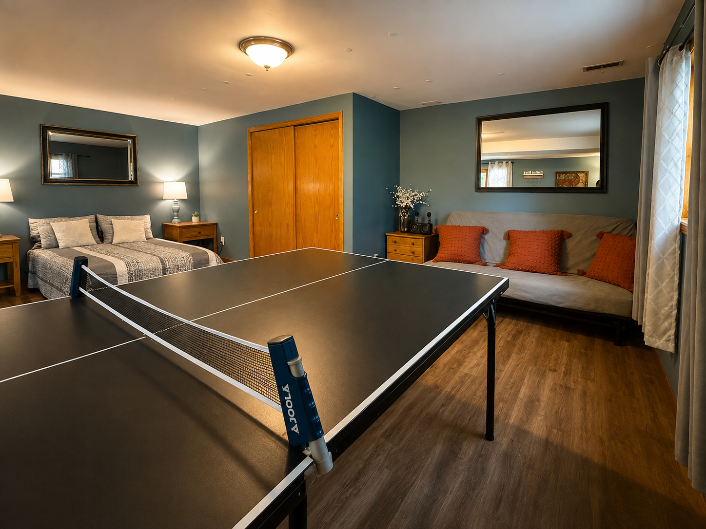 Basement rec room with a ping-pong table, bed, couch, and warm lighting