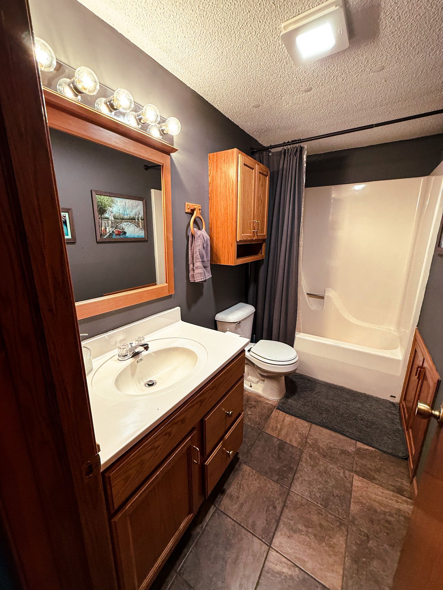 Small bathroom with vanity, mirror lights, toilet, and bathtub in gray and wood tones