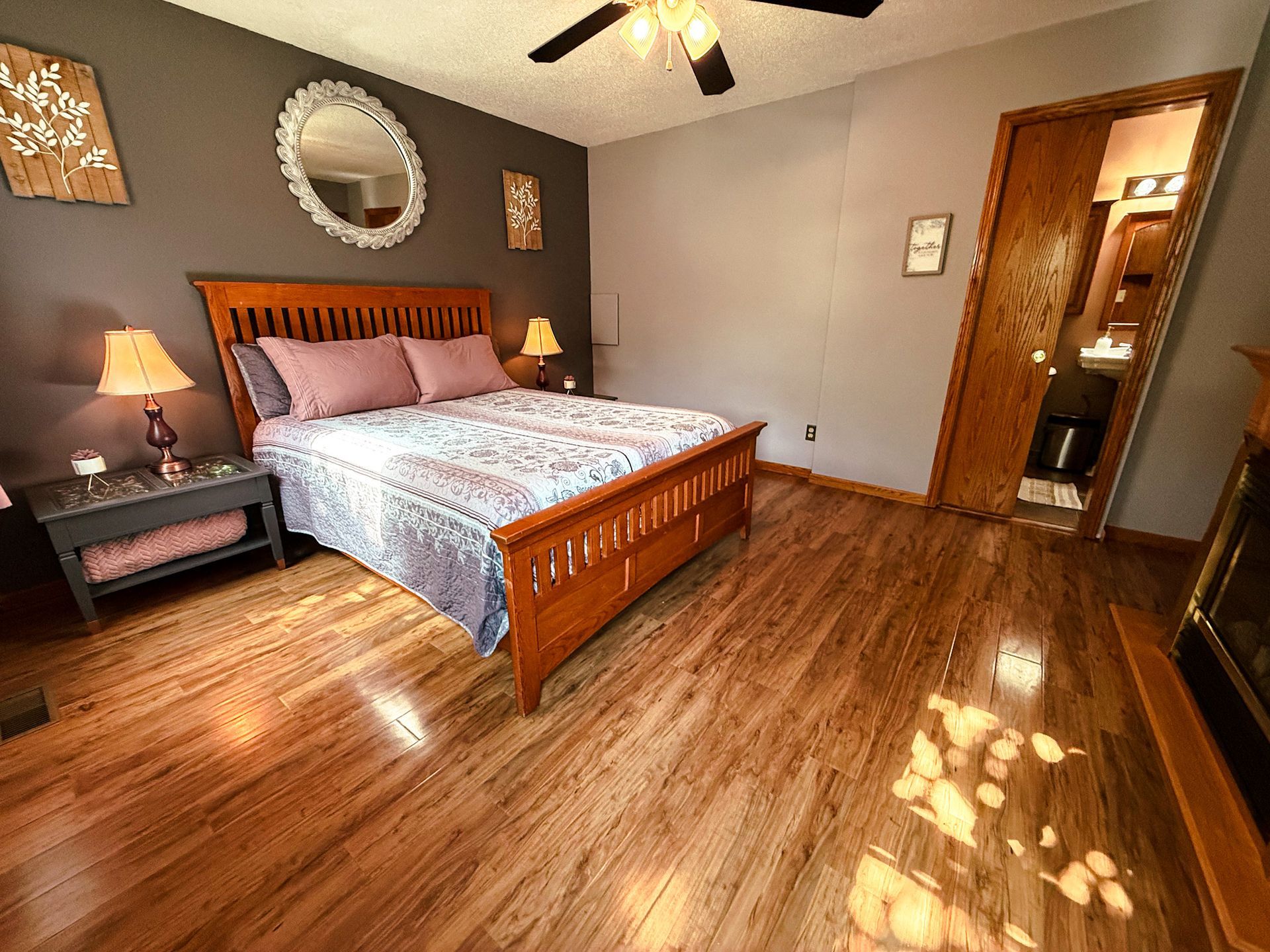Bedroom with wooden bed, hardwood floors, ceiling fan, and sunlight streaming through the window.