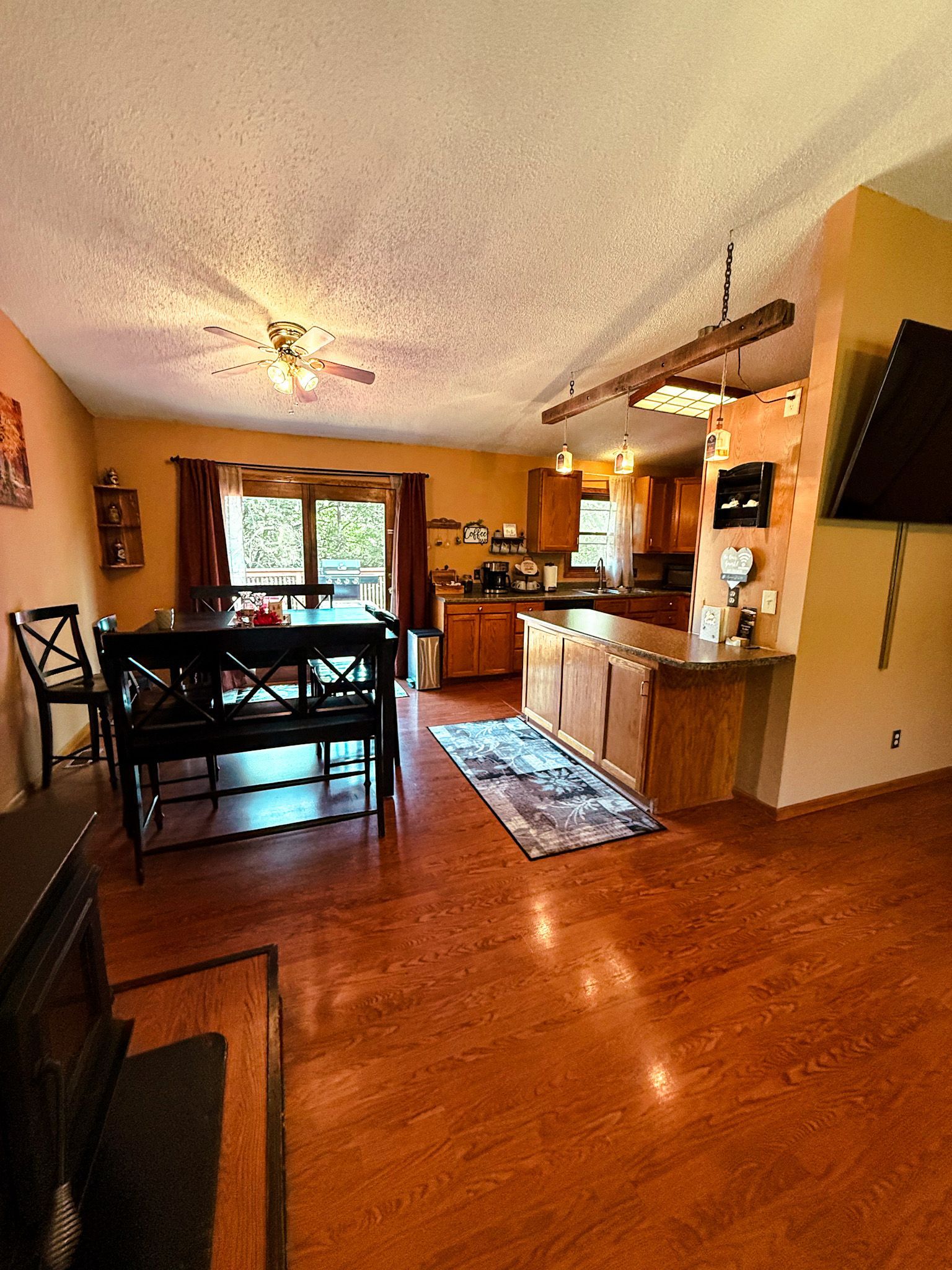 Open kitchen and dining area with wooden floors, table, cabinets, and sliding glass doors.