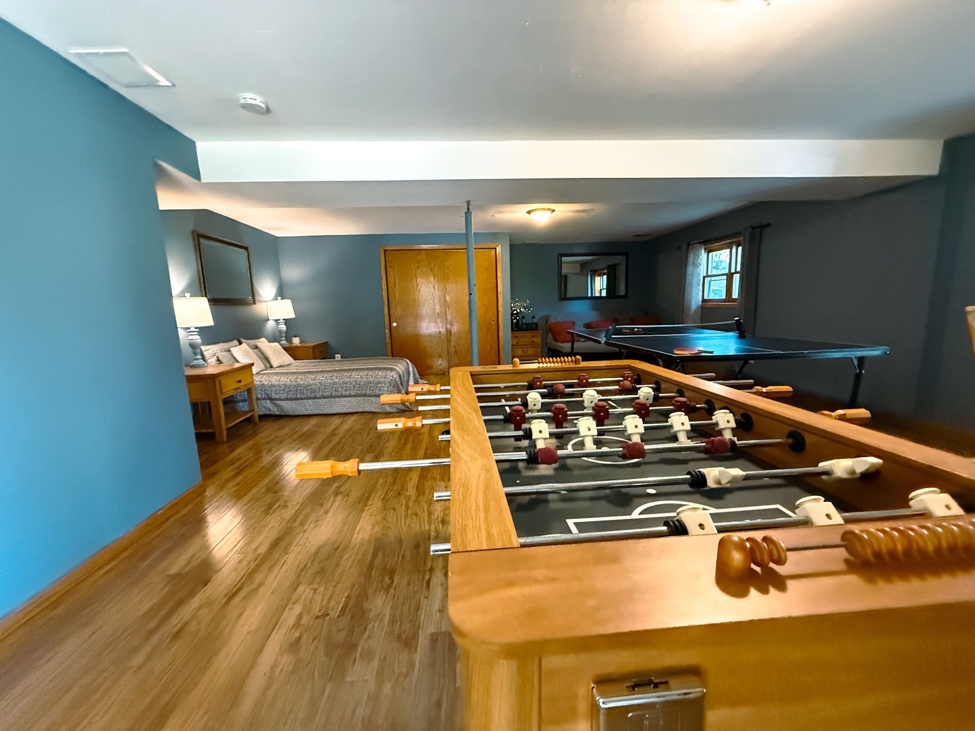 Indoor game room with blue walls, foosball table, pool table, and a bed in the background