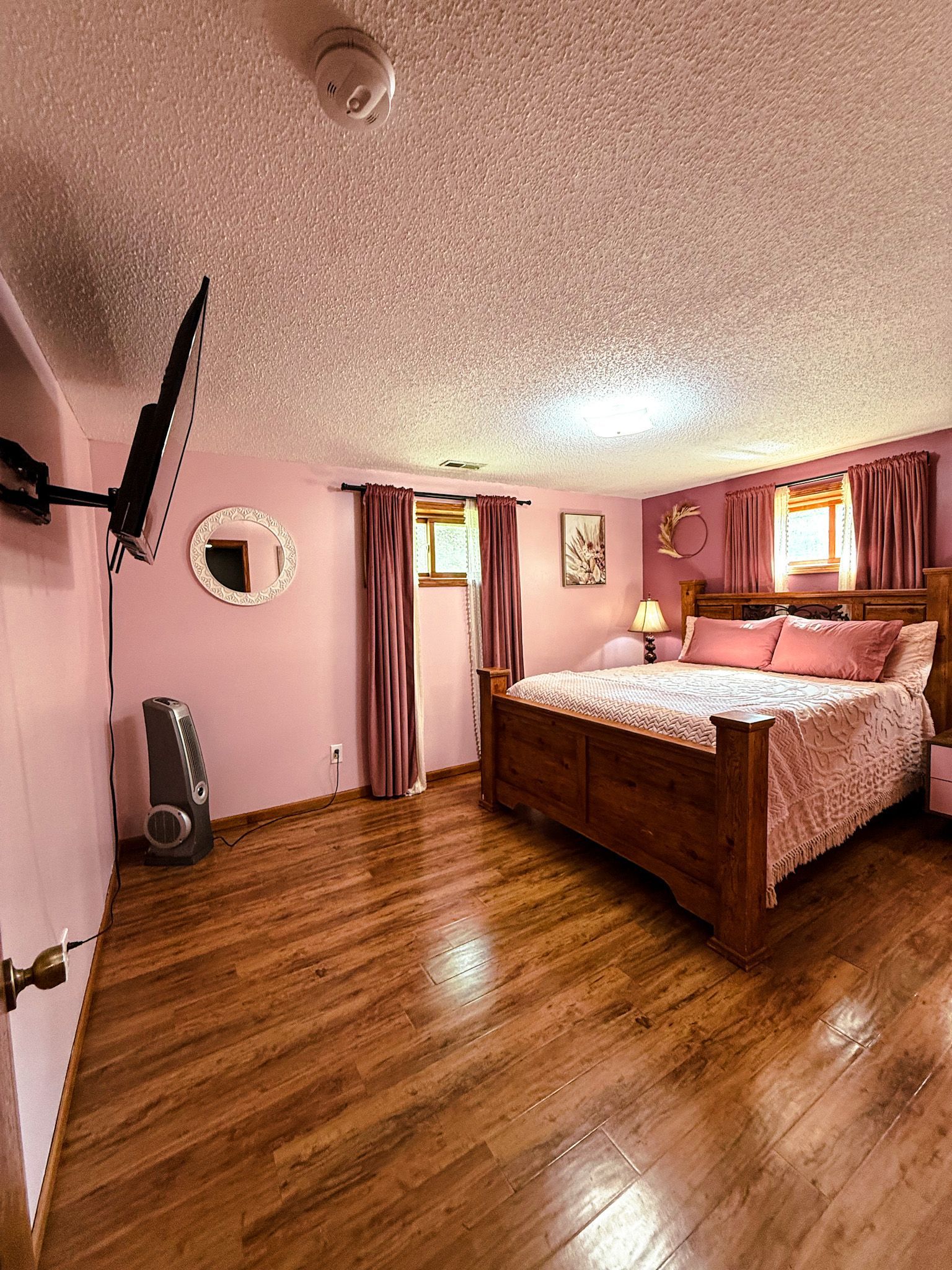 Pink bedroom with wooden bed, hardwood floors, and curtained window light