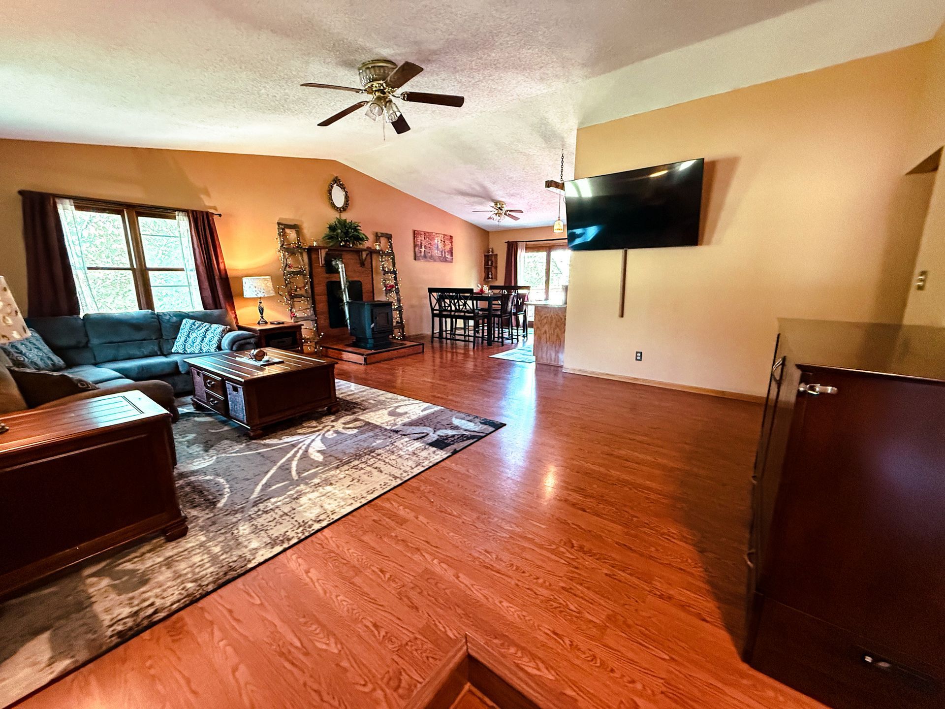 Spacious living room with leather seating, wall-mounted TV, ceiling fan, and hardwood floors.