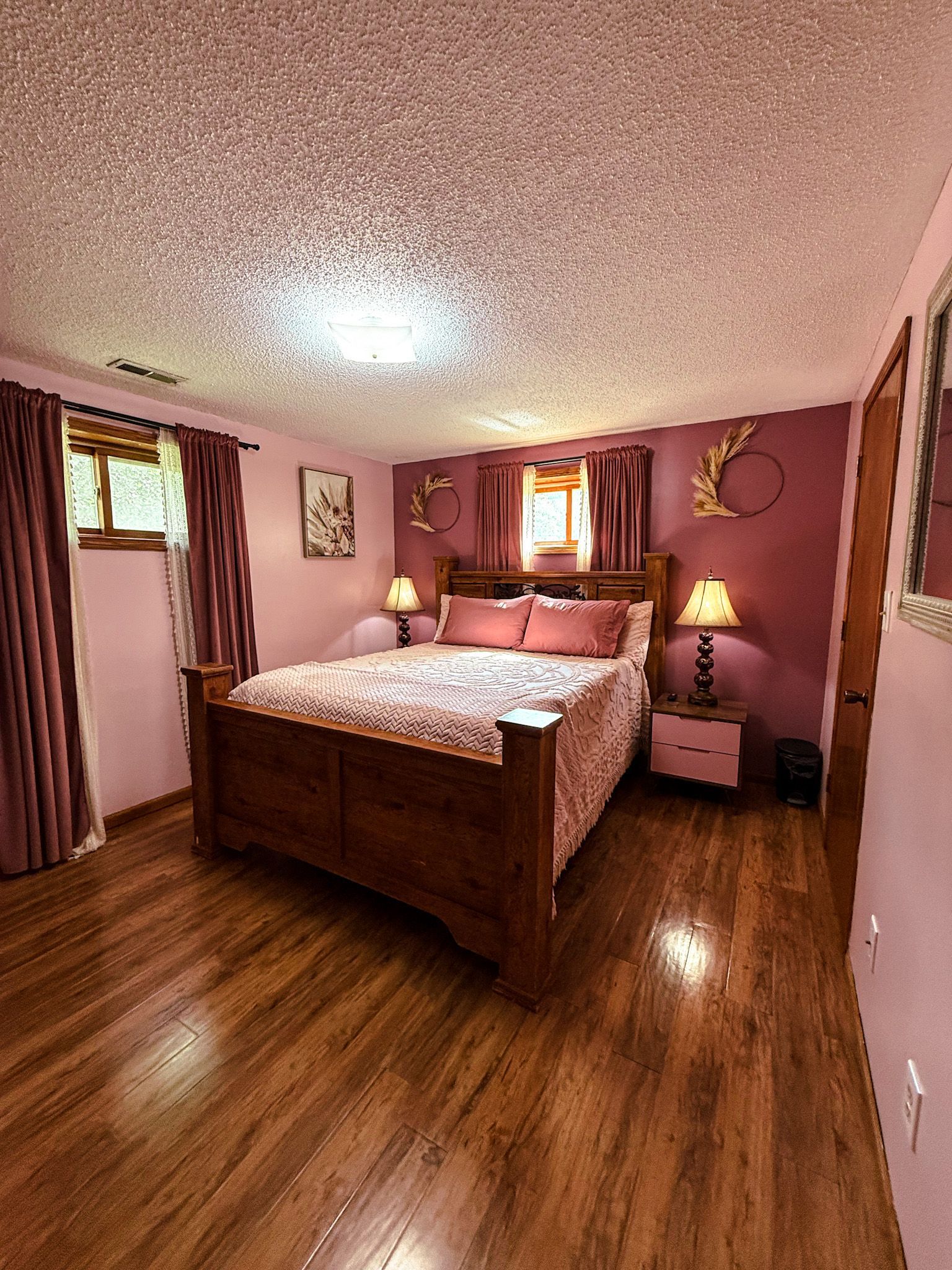 Cozy pink bedroom with wooden bed, floral bedding, lamps, and hardwood floors