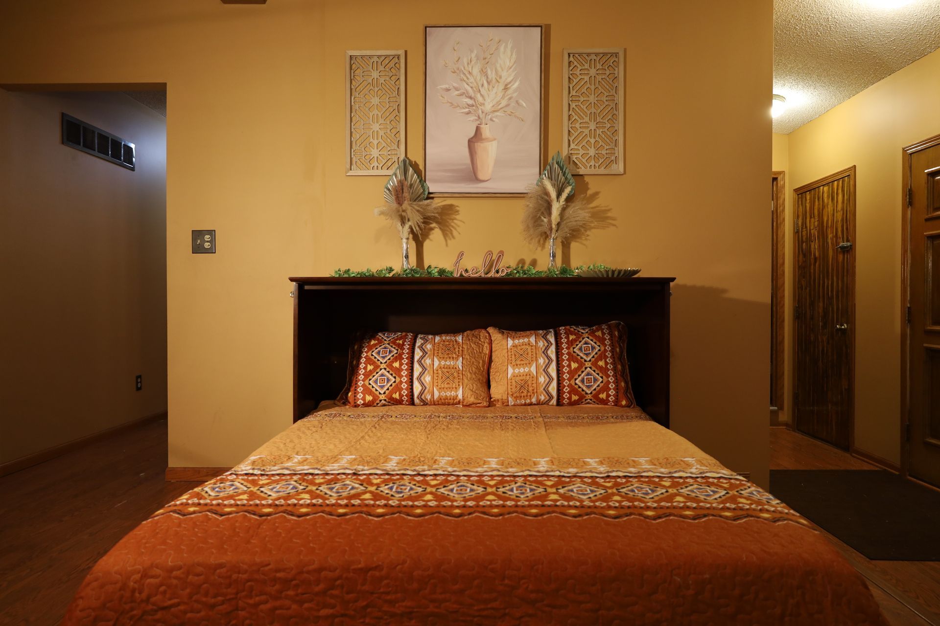 Murphy bed with patterned bedding in a warmly lit bedroom with wall art and decorative accents