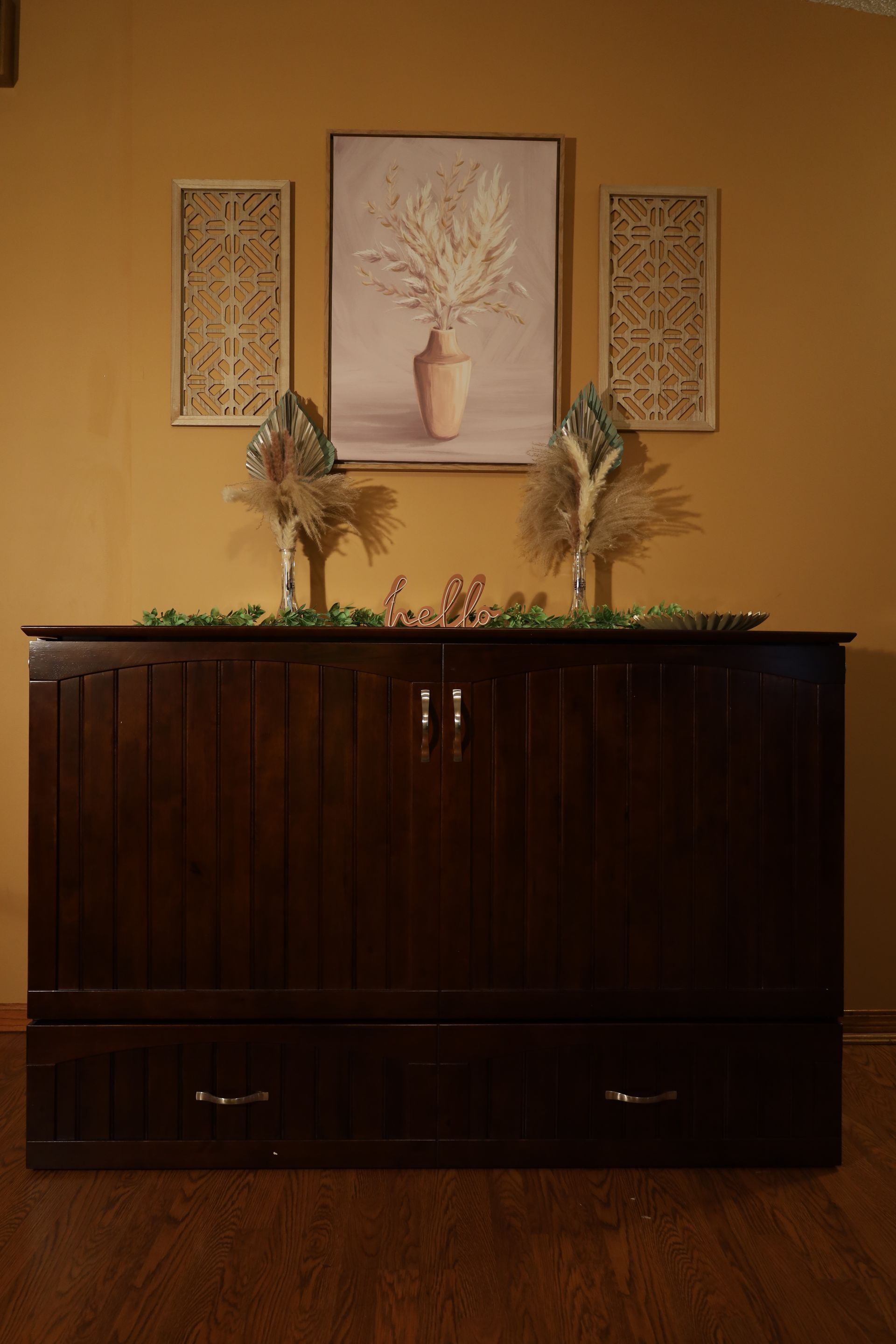 Dark wood sideboard with floral decor and framed wall art against a tan wall.