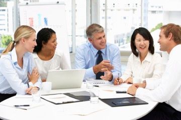 A group of people are sitting around a table with laptops.