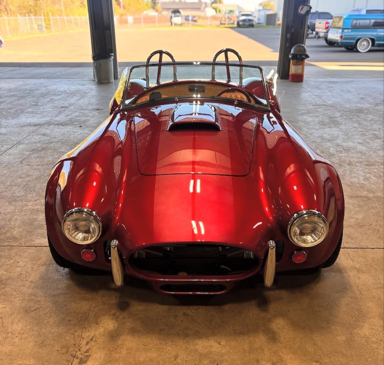 Red Shelby Cobra roadster parked inside, showcasing glossy paint and chrome details.