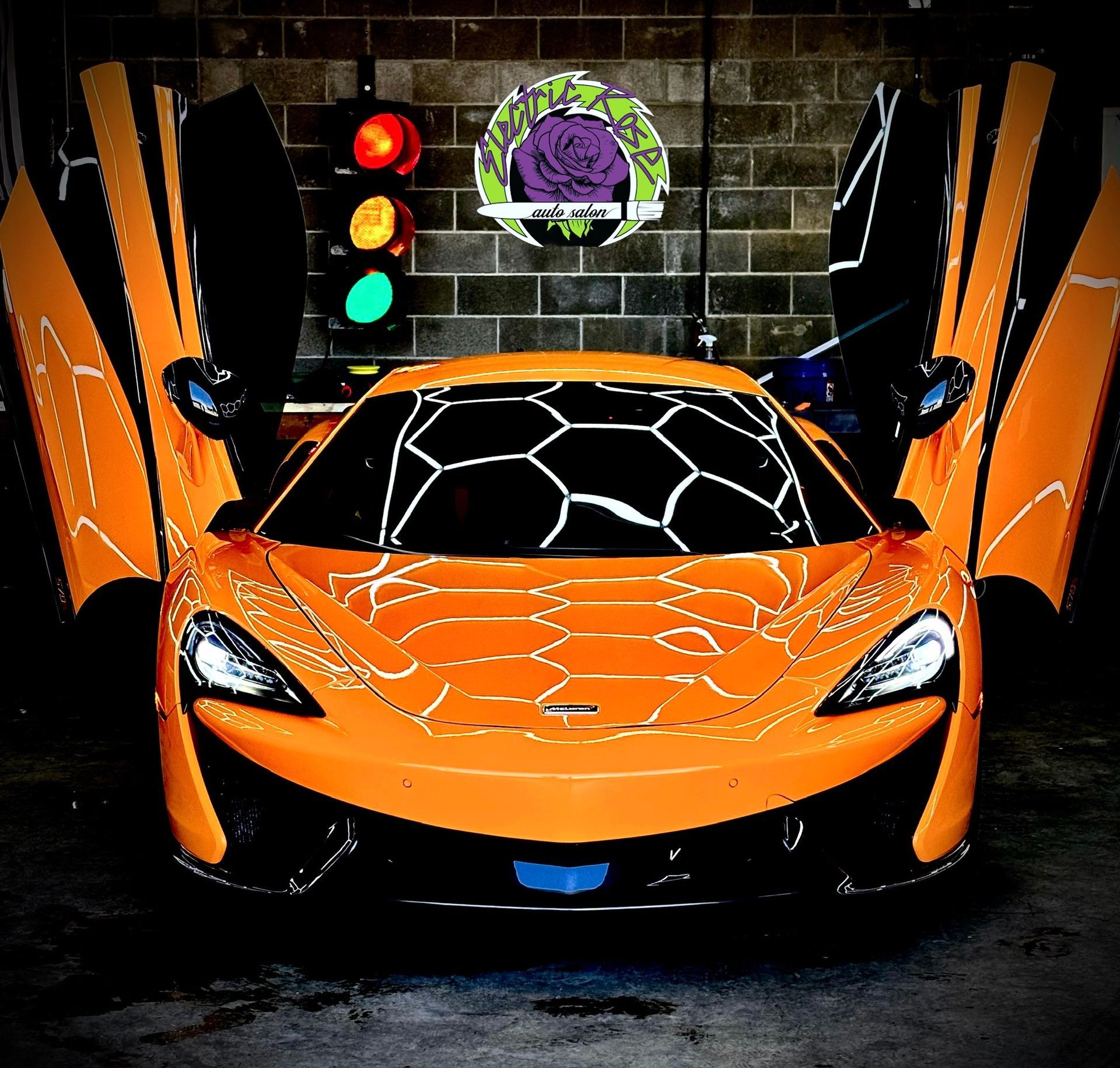 Orange McLaren sports car with open doors in a garage, beneath a traffic light.