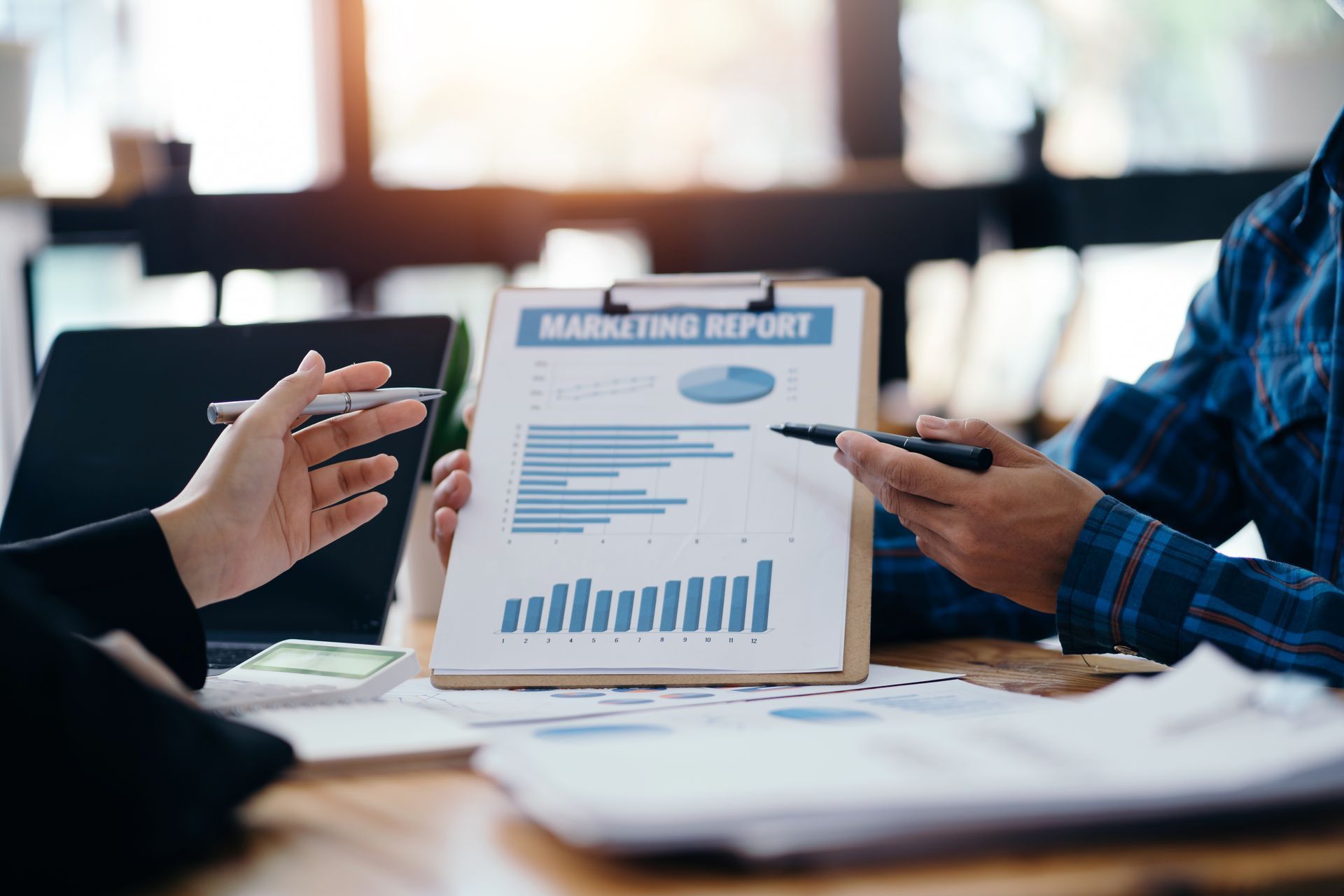 A man and a woman are looking at a marketing report on a clipboard.