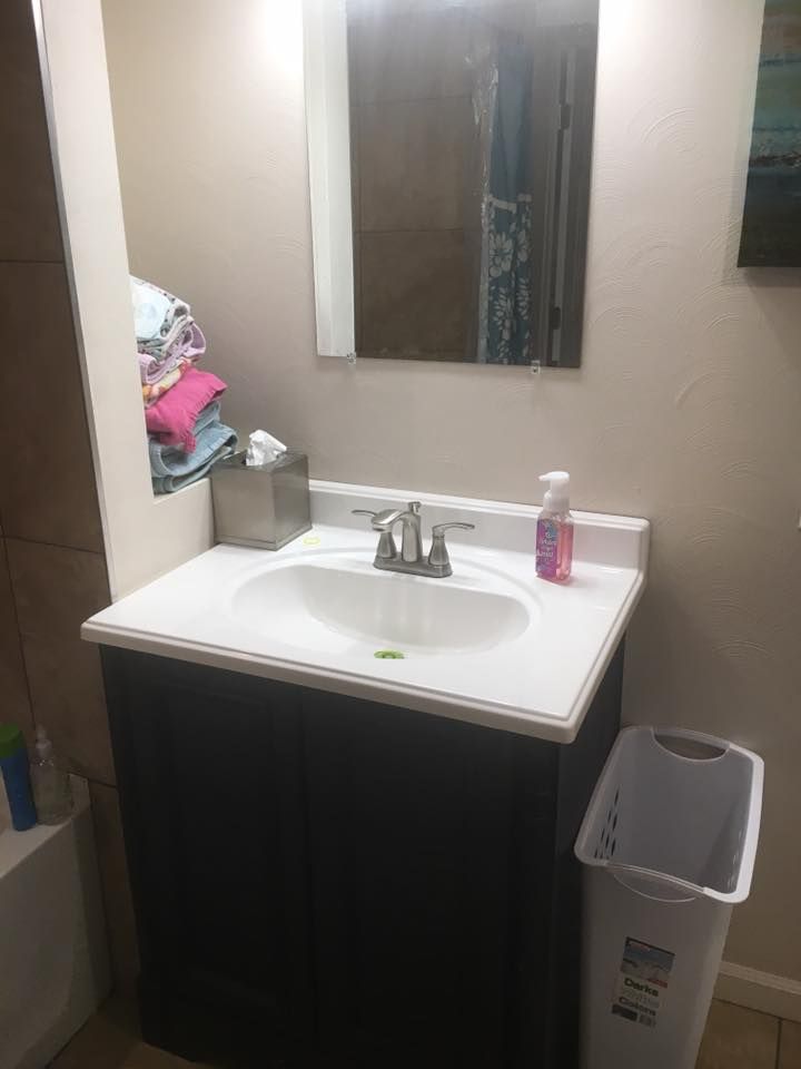 A bathroom with a sink , mirror and trash can.