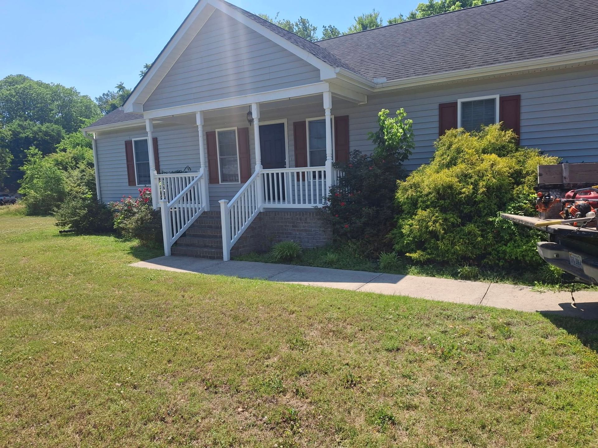 Single-story house with a front porch, white railings, and a lawn in bright sunlight