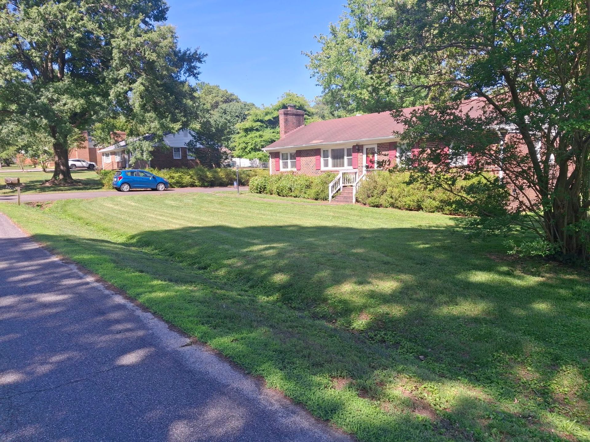 Suburban house with red roof beside a grassy yard and driveway under sunny trees