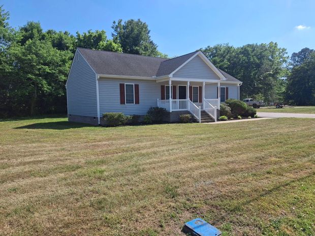 Small white house with a front porch and a large mowed lawn under a clear blue sky
